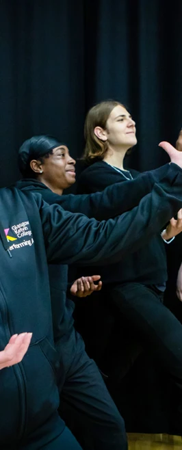 A lecturer and students striking dramatic poses against a black curtain, smiling and enjoying their creative acting activity. A lecturer and students striking dramatic poses against a black curtain, smiling and enjoying their creative acting activity.